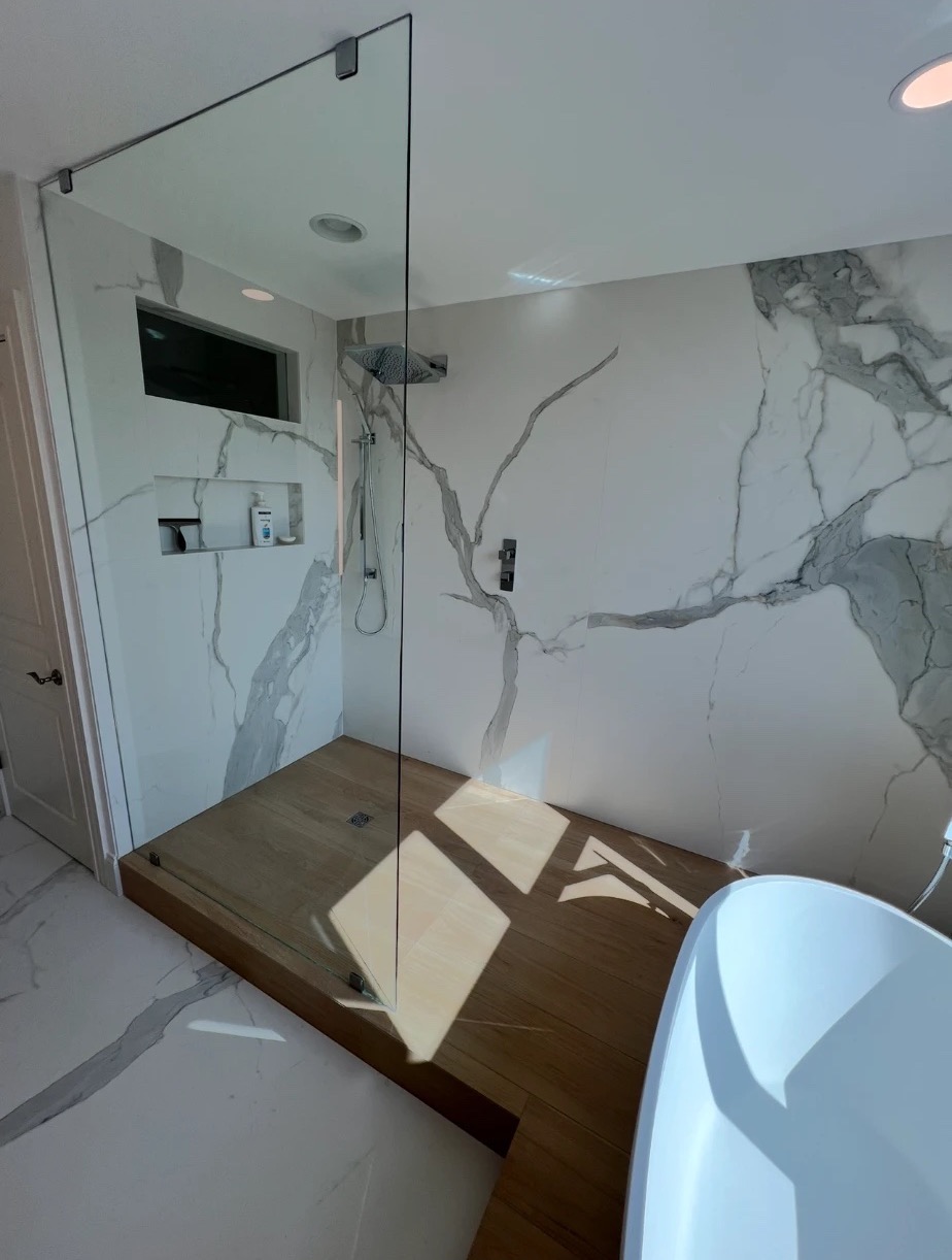 Walk-in shower with frameless glass, slab walls and wood-look tile platform