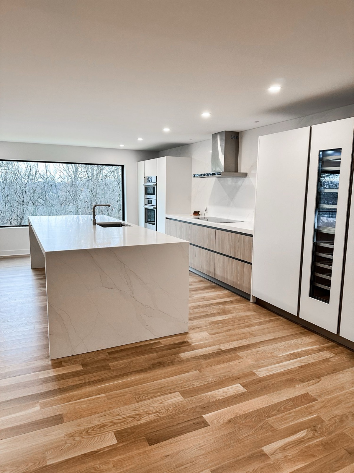 New white oak hardwood floors running through an open kitchen with a waterfall island